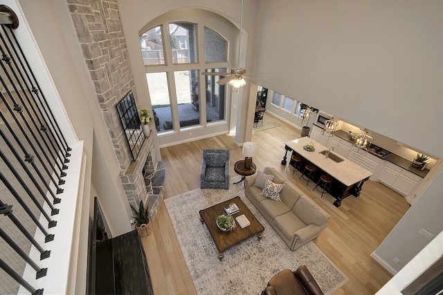 living room featuring a stone fireplace, hardwood / wood-style floors, a towering ceiling, and ceiling fan with notable chandelier