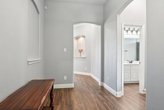 corridor with arched walkways, dark wood-style flooring, a sink, and baseboards