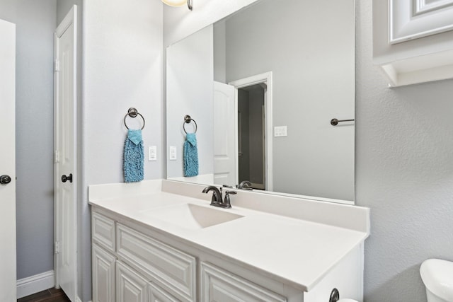 half bathroom with baseboards, vanity, and toilet