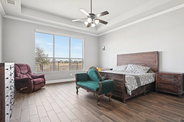 bedroom with a tray ceiling, crown molding, visible vents, a ceiling fan, and wood finished floors