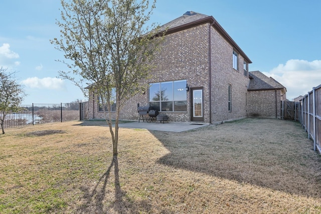 back of house featuring a patio, brick siding, a lawn, and a fenced backyard