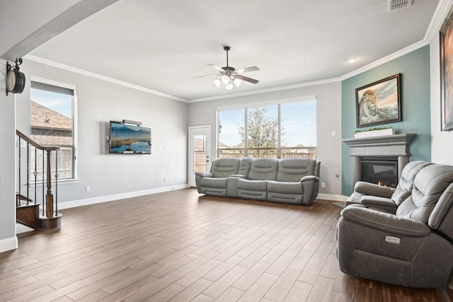 living room featuring a wealth of natural light, a glass covered fireplace, stairway, and wood finished floors