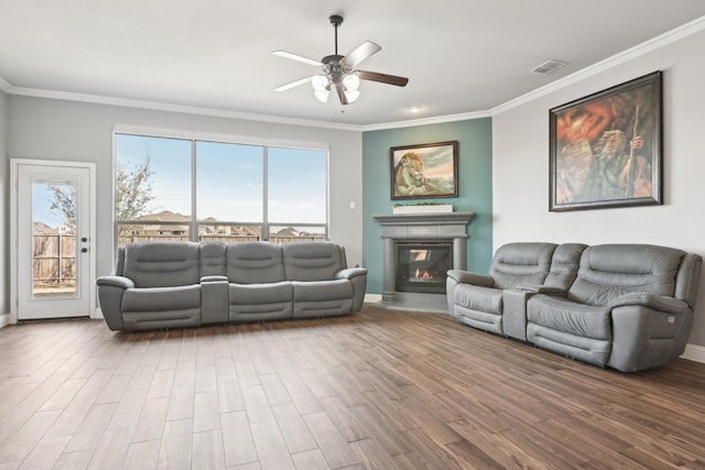 living room featuring ornamental molding, a glass covered fireplace, wood finished floors, and visible vents