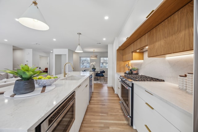 kitchen with stainless steel appliances, sink, white cabinets, decorative backsplash, and hanging light fixtures