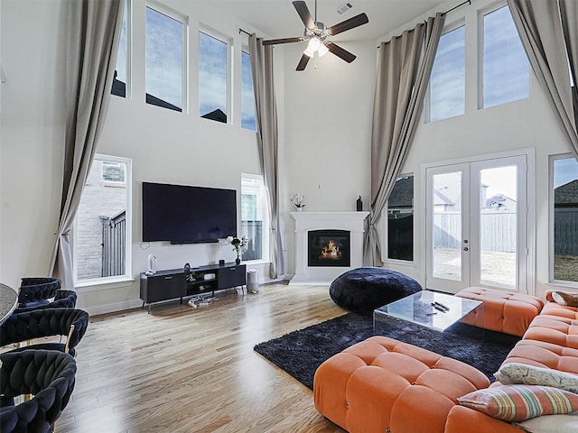 living room featuring light hardwood / wood-style floors, ceiling fan, french doors, and a towering ceiling