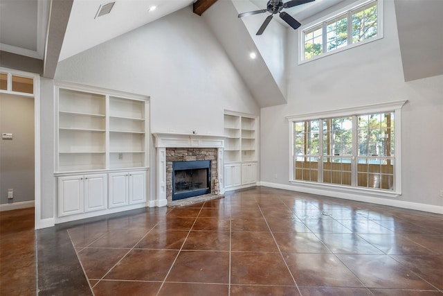 unfurnished living room with a high ceiling, a stone fireplace, ceiling fan, built in features, and beam ceiling