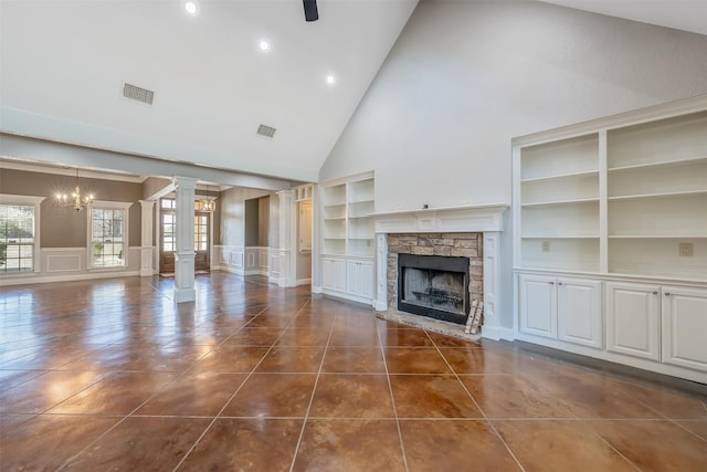 unfurnished living room featuring a towering ceiling, ornate columns, built in shelves, a notable chandelier, and a fireplace