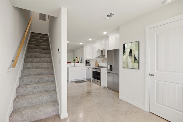 kitchen featuring white cabinetry, wall chimney range hood, stainless steel appliances, and sink