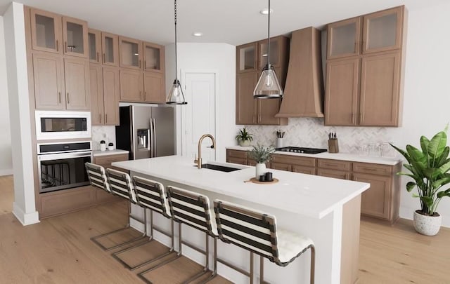 kitchen with sink, hanging light fixtures, stainless steel appliances, an island with sink, and light hardwood / wood-style floors