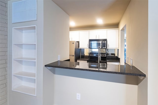 kitchen with dark stone counters, kitchen peninsula, white cabinetry, and stainless steel appliances