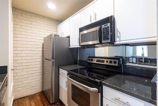 kitchen with dark stone countertops, dark hardwood / wood-style flooring, white cabinetry, stainless steel appliances, and brick wall