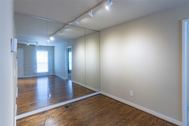 empty room featuring rail lighting and dark wood-type flooring