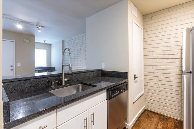 kitchen with dark stone counters, rail lighting, sink, appliances with stainless steel finishes, and white cabinetry