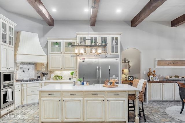 kitchen with a kitchen bar, tasteful backsplash, built in appliances, a kitchen island, and custom range hood