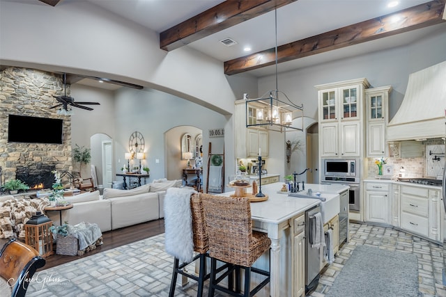 kitchen featuring a breakfast bar area, hanging light fixtures, stainless steel appliances, a fireplace, and an island with sink