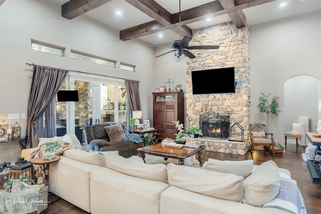 living room featuring dark wood-type flooring, ceiling fan, beam ceiling, a towering ceiling, and a fireplace