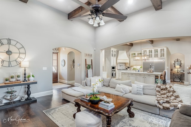 living room with beamed ceiling, a high ceiling, dark hardwood / wood-style floors, and ceiling fan