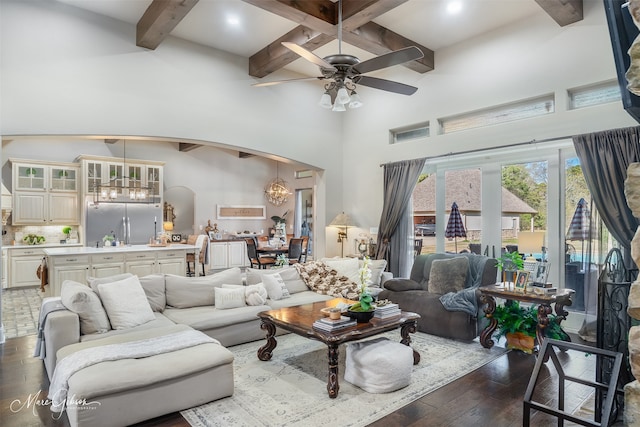 living room featuring a high ceiling, dark hardwood / wood-style floors, ceiling fan with notable chandelier, and beam ceiling