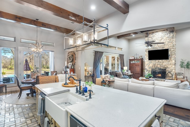 kitchen featuring ceiling fan with notable chandelier, a fireplace, decorative light fixtures, beamed ceiling, and a center island with sink