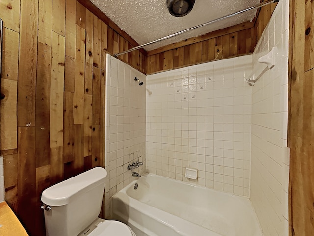 bathroom featuring wooden walls, tiled shower / bath, a textured ceiling, and toilet