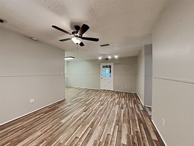 unfurnished room with a textured ceiling, rail lighting, ceiling fan, and hardwood / wood-style floors