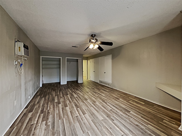 unfurnished bedroom featuring a textured ceiling, two closets, ceiling fan, hardwood / wood-style flooring, and an AC wall unit