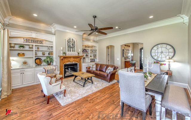 living room featuring built in shelves, light hardwood / wood-style flooring, ceiling fan, and crown molding