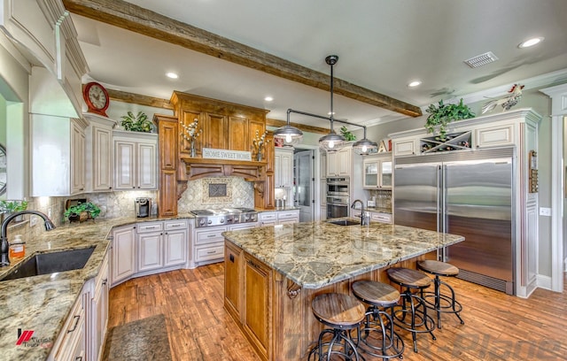 kitchen featuring decorative backsplash, appliances with stainless steel finishes, sink, beam ceiling, and an island with sink