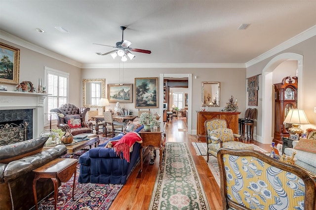 living room with a high end fireplace, light wood-type flooring, ceiling fan, and crown molding