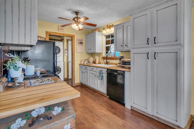 kitchen featuring sink, light wood-type flooring, black dishwasher, ceiling fan, and stacked washing maching and dryer