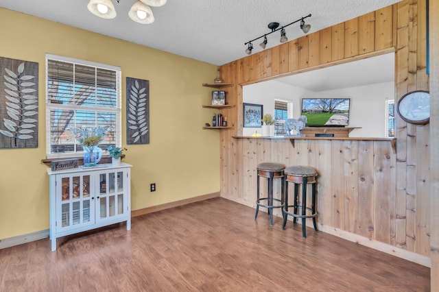 kitchen with hardwood / wood-style flooring, a textured ceiling, a kitchen bar, kitchen peninsula, and wood walls