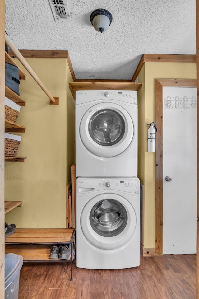 clothes washing area with hardwood / wood-style flooring, stacked washing maching and dryer, a textured ceiling, and crown molding