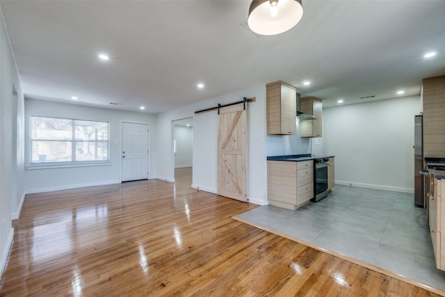 kitchen featuring oven, a barn door, light wood-type flooring, light brown cabinetry, and stainless steel refrigerator