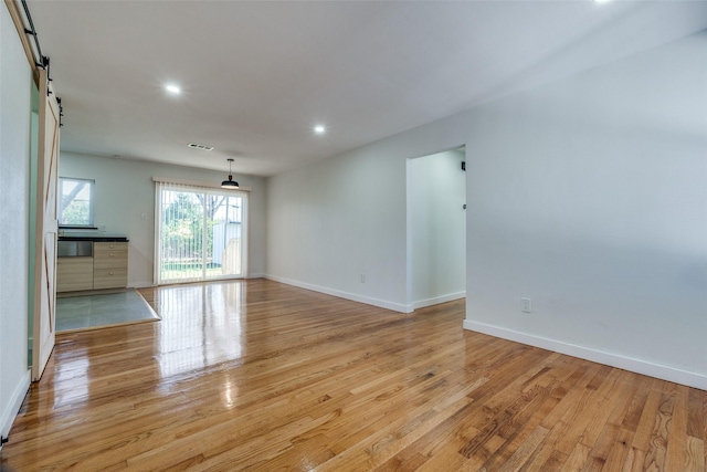 unfurnished living room with a barn door and light hardwood / wood-style floors