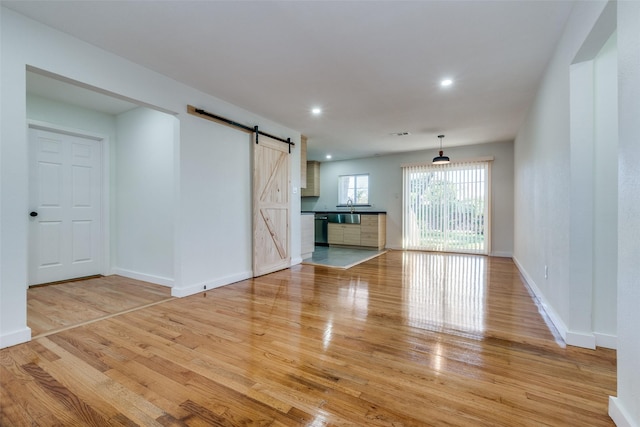 unfurnished living room with a barn door, light hardwood / wood-style flooring, and sink