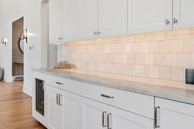 kitchen featuring white cabinetry, backsplash, light stone countertops, beverage cooler, and light wood-type flooring