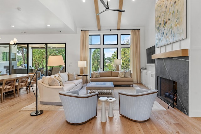 living room with ceiling fan, a high end fireplace, beam ceiling, and light hardwood / wood-style flooring