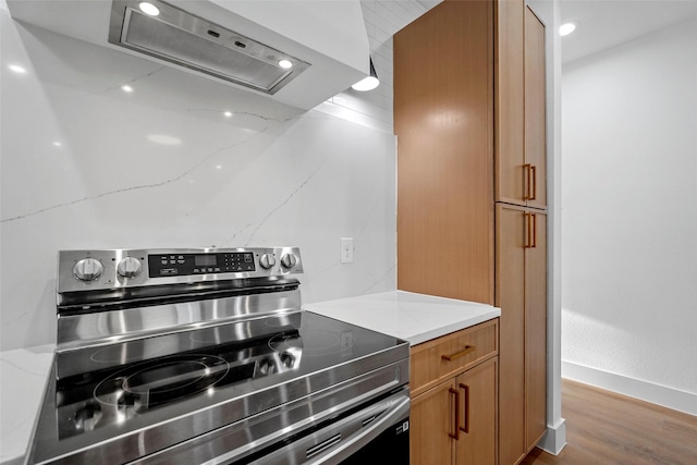 kitchen featuring electric range, light stone countertops, range hood, and light hardwood / wood-style floors