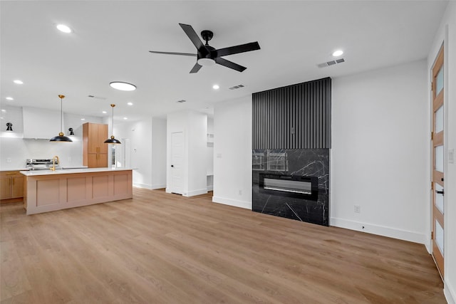 unfurnished living room featuring a high end fireplace, light hardwood / wood-style floors, ceiling fan, and sink