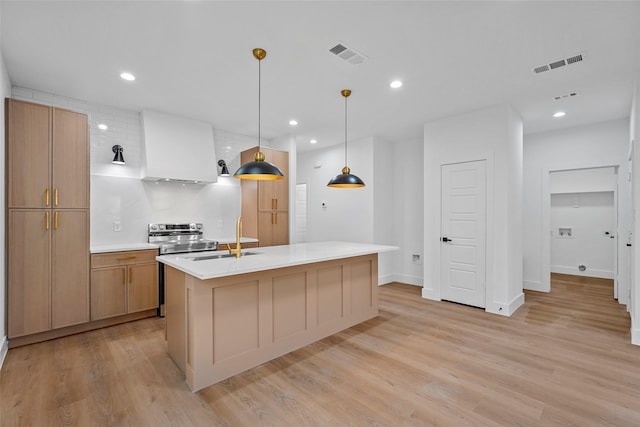 kitchen with decorative backsplash, light wood-type flooring, a kitchen island with sink, sink, and hanging light fixtures