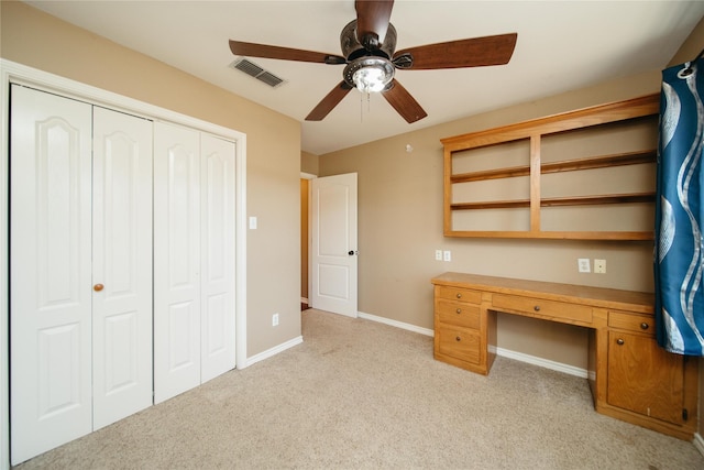 unfurnished office featuring ceiling fan, light colored carpet, and built in desk