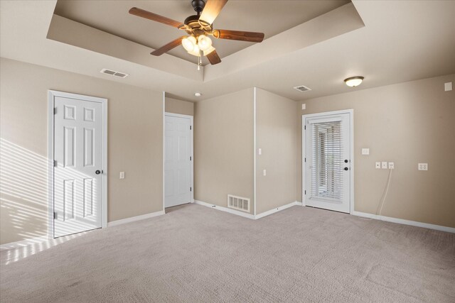 carpeted spare room with a tray ceiling and ceiling fan