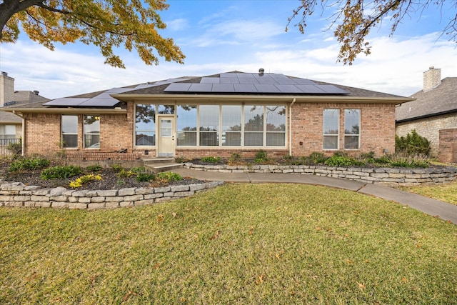 rear view of property featuring a lawn and solar panels