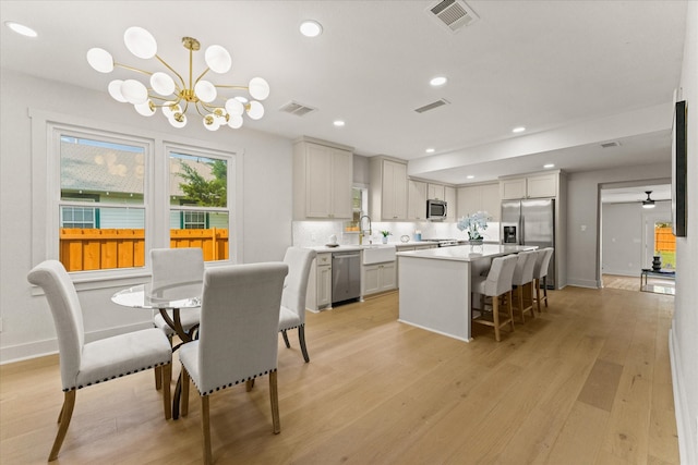 dining room with sink, light hardwood / wood-style floors, and ceiling fan with notable chandelier