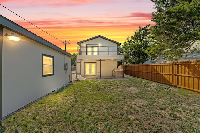 back house at dusk with a lawn, ceiling fan, french doors, a balcony, and a patio