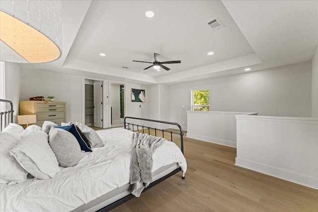 bedroom with ceiling fan, a tray ceiling, and hardwood / wood-style floors