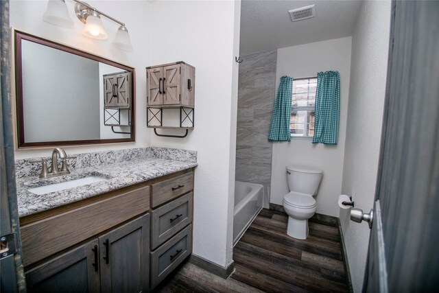 full bathroom featuring vanity, wood-type flooring, a textured ceiling, shower / washtub combination, and toilet