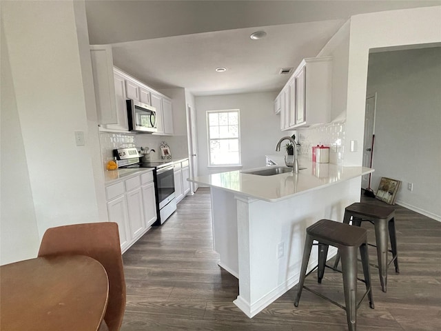 kitchen featuring kitchen peninsula, a kitchen breakfast bar, stainless steel appliances, sink, and white cabinets