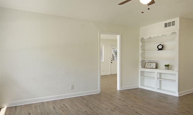 unfurnished room featuring hardwood / wood-style flooring, ceiling fan, and built in shelves