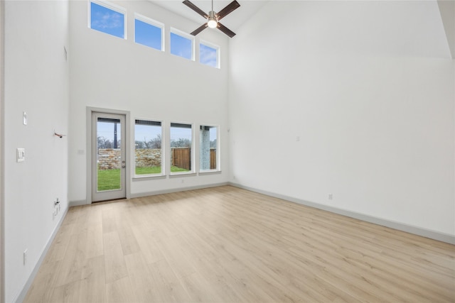 unfurnished living room with a high ceiling, plenty of natural light, ceiling fan, and light wood-type flooring